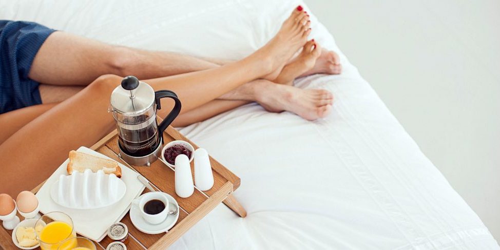 Man and woman intertwining legs with coffee in bed