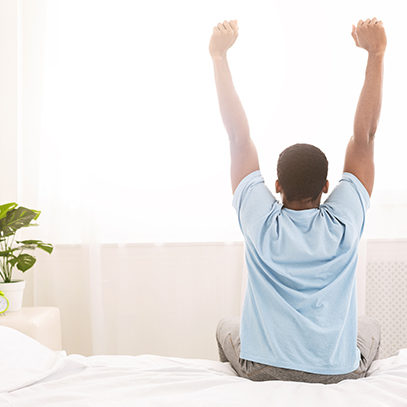 Young man waking up in bed and stretching his arms