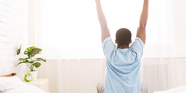 Young man waking up in bed and stretching his arms